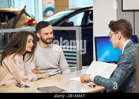 young couple choosing a car in the car canter, close up photo, young man in elegant grey suit having a business conversation with family Stock Photo