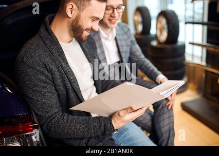 happy man enjoying buying process at dealership, bargain, successful shopping, man and shop assistant having fun at the garage Stock Photo