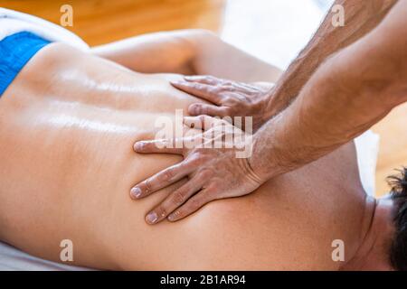 A man receiving massage treatment. Close-up of masseur hands and a client back. Man getting a relaxing massage in the spa Stock Photo