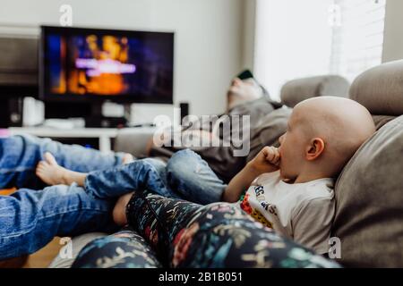 Family relaxing on couch watching tv while dad naps Stock Photo