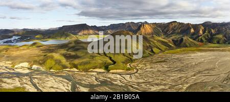 Amazing drone view of arid riverbed and green hills located near river against cloudy sky in Iceland Stock Photo
