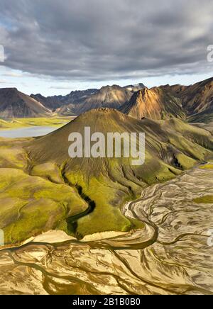 Breathtaking drone view of green mountains and dry riverbed located against stormy cloudy sky in Iceland Stock Photo