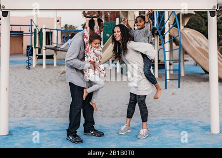 Happy family playing outside at park playground at dusk Stock Photo