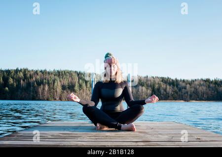 woman meditating in a wetsuit at the beach before cold water swimming