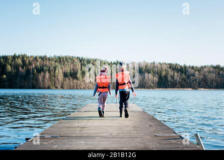 brother and sister walking along a pier in winter with life vests on
