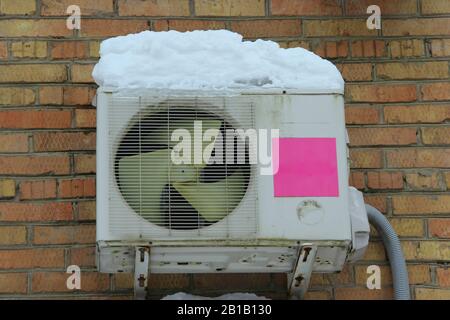 White air conditioning part of a split system hanging on a brick wall of a building covered in snow and icicles in winter in Russia. Stock Photo