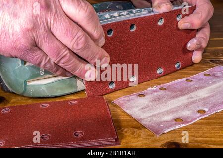 A man’s hands attaching a new self adhesive sheet onto an orbital power sander, having removed the worn out sheet nearby. Stock Photo