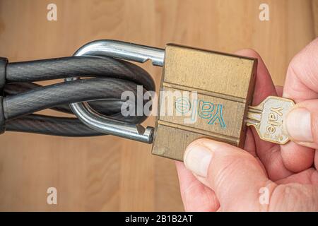 A man’s hands unlocking a Yale key operated padlock, through dual hooped ends of a vinyl coated, braided steel, security cable. Stock Photo