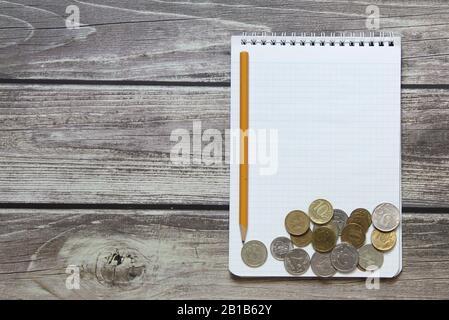 Notepad with a blank white sheet in a checker paper with russian coins and pencil lies on the background of wooden boards Stock Photo