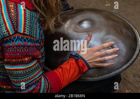 A native musician is seen close up, using hand to beat a hang metal pan drum outdoors during a festival celebrating traditional culture and earth Stock Photo