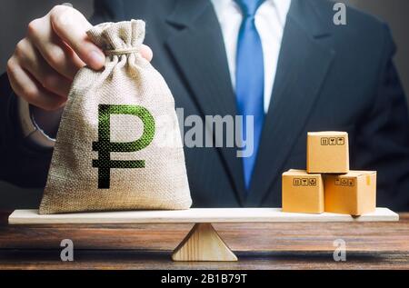 Businessman puts a russian ruble money bag and bunch of boxes on scales. Trade exchange balance. Retail distribution. Trade balance. Import export, ec Stock Photo