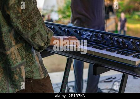 A closeup and cropped shot in selective focus on the hands of a man playing an electronic keyboard synthesizer, with a band on stage at earth festival Stock Photo