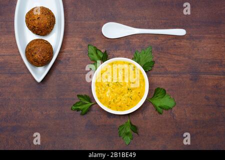 Chickpea falafel is lying in an almond-shaped bowl, beside is a ceramic spoon and a bowl with tahini sauce with turmeric and minced parsley leaves. Stock Photo