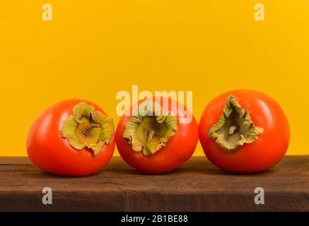 Fresh ripe persimmons. Persimmons on yellow background. Хурма. Stock Photo