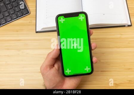 Mockup image of hand holding black mobile phone with green screen in the office table on the background Stock Photo