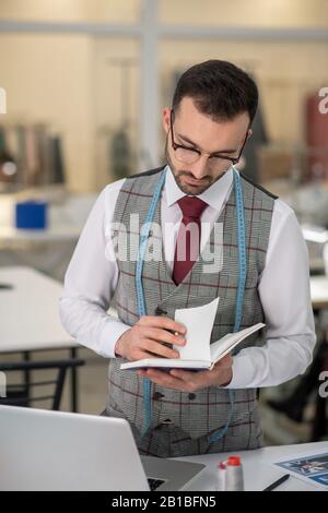 Young male tailor checking his notes on tablet computer when drawing ...