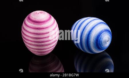 Colored streaked handmade Easter eggs. Still life with reflection on shiny black background. Close-up of standing pink and lying blue ornate egg shell. Stock Photo