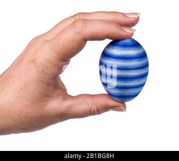 Blue striped Easterr egg in female fingers isolated on white background. Human hand closeup holding original holiday decoration coated by thin yarn. Stock Photo