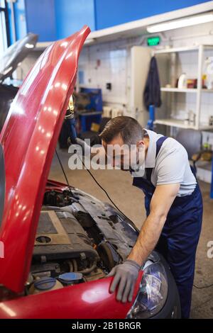 High angle view at bearded car mechanic looking under hood during vehicle inspection in garage shop, copy space Stock Photo