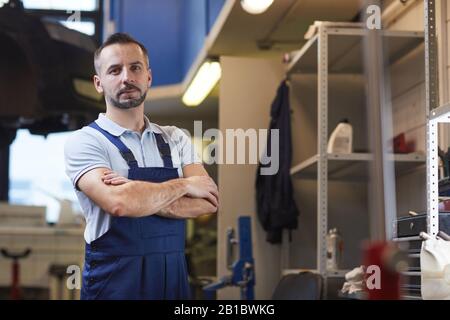 Waist up portrait of muscular car mechanic standing with arms crossed while posing in garage shop, copy space Stock Photo