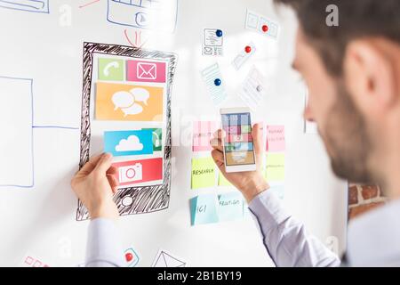 Designer man drawing website ux app development and holding smart phone on hand. User experience concept. Stock Photo