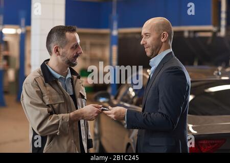 Waist up portrait of mechanic giving keys to mature businessman after checking luxury car at annual inspection, copy space Stock Photo