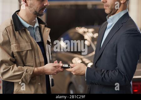 Mid section of mechanic giving car keys to businessman after checking luxury car at annual inspection in auto repair shop, copy space Stock Photo