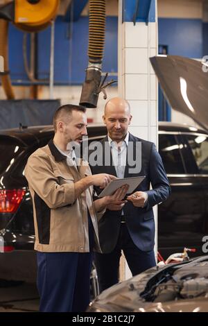 Mechanic and customer inspecting car in auto repair shop Stock Photo ...