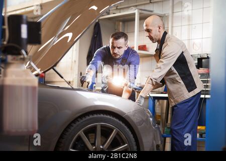 Portrait of two car mechanics looking under hood of car in auto repair workshop, copy space Stock Photo