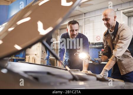 Waist up portrait of two car mechanics looking under hood of car in auto repair workshop, copy space Stock Photo