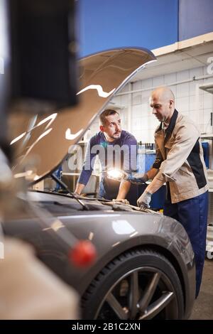 Full length portrait of two car mechanics looking under hood of car in auto repair workshop, copy space Stock Photo