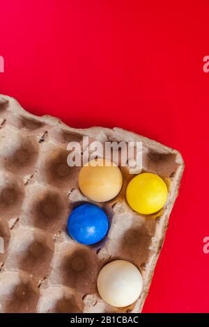An egg carton with four pastel dye easter eggs on the red paper background. Vertical image. Happy Easter concept Stock Photo