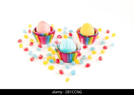 Bright creative Easter decoration of colorful eggs in raibow colored paper forms for cupcakes on white background decorated with jelly candies. Mockup Stock Photo