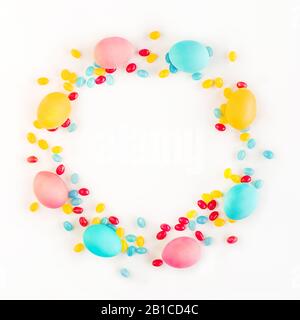 Colorful Easter wreath made of yellow tulips, colorful eggs and candies on white background. Flat lay style. Backdrop for your design. Copy space. Stock Photo