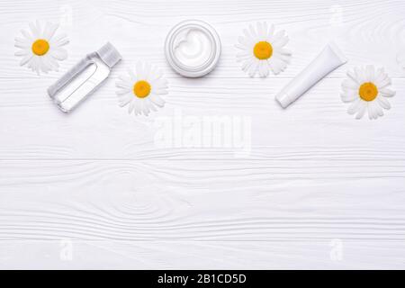 Bottles with cosmetics and daisy flowers on white wooden background. Cream, tonic, water and facial scrub. White tubes. Mockup natural cosmetic produc Stock Photo