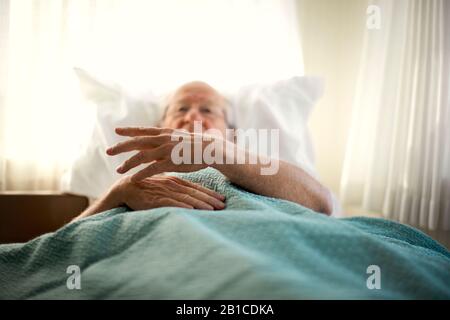 Senior man gesturing with his hand while lying in bed in his bedroom. Stock Photo