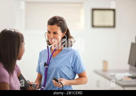 Smiling female doctor taking a teenage girl's blood pressure with a sphygometer inside a doctor's office. Stock Photo