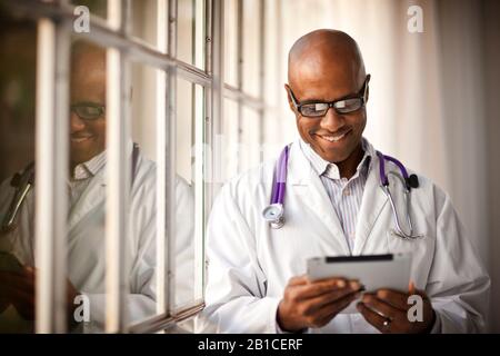 Laughing male doctor looking at an iPad while standing next to a window. Stock Photo