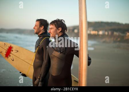 Smiling friends standing with surfboards on a beach. Stock Photo