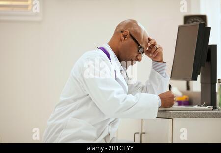 Focused male doctor taking notes while sitting inside his office. Stock Photo