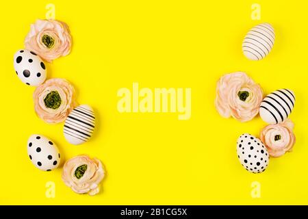 Frame of creative graphic eggs and ranunculus flowers on bright yellow background. Easter concept. Place for text. Stock Photo