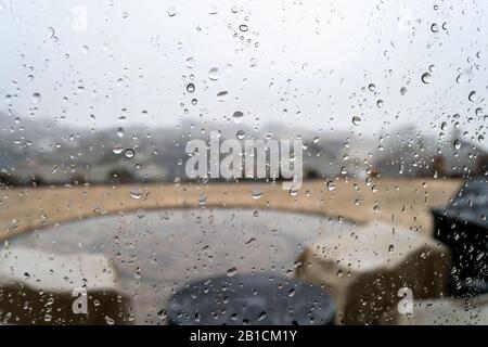 View from inside a hilltop home of a patio and subdivision below as rain falls. Taken through a rain covered and water spotted window . Stock Photo