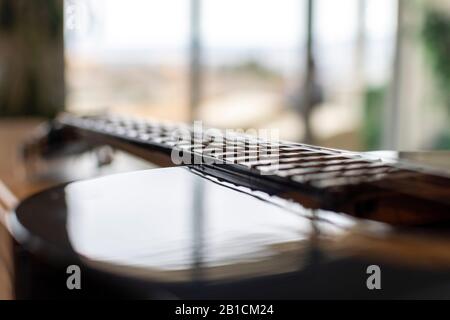 Selective focus on the neck, frets and strings of a guitar with blurred bokeh background of a window letting light in. Stock Photo