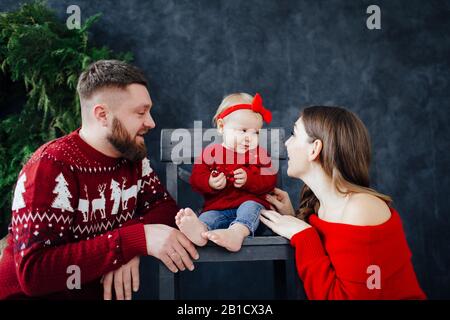 Family in red sweater kiss the heels of the baby. Stock Photo