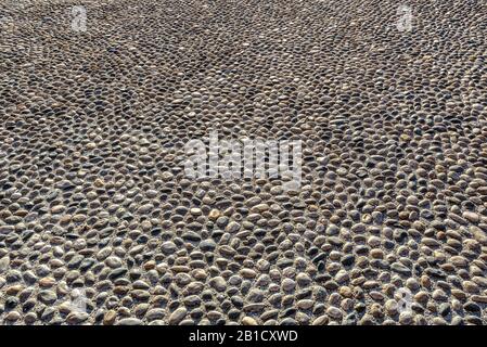 Cobblestone road background. Stone pavement in perspective. Old street paved with rocks. Paving ground close-up in summer. Texture of floor with pebbl Stock Photo