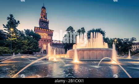 Panoramic view of Sforza Castel (Castello Sforzesco) with lighting fountain at night, Milan, Italy. This castle was built in the 15th cent by Sforza, Stock Photo