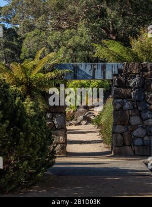 Garden path with rock feature wall, arch doorway along stone walkway surrounded by trees Stock Photo