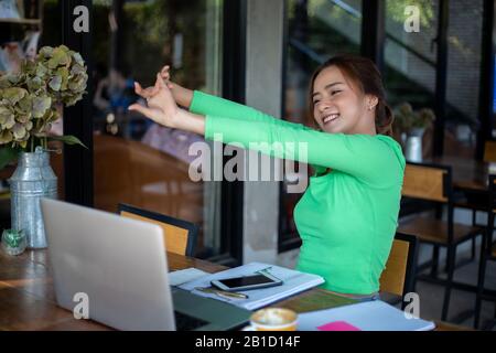Asian woman stretching after reading book and work hard and smiling in coffee shop Stock Photo