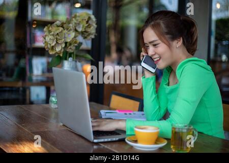 Asian Business women are using mobile and touch smart phone for Communication and women using notebook for working in coffee shop Stock Photo