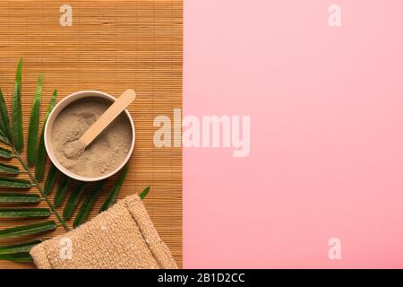 Natural skin care products at home. Gray clay in a jar brush sponge made of natural eco-friendly material on a pink background with green leaves. Hori Stock Photo